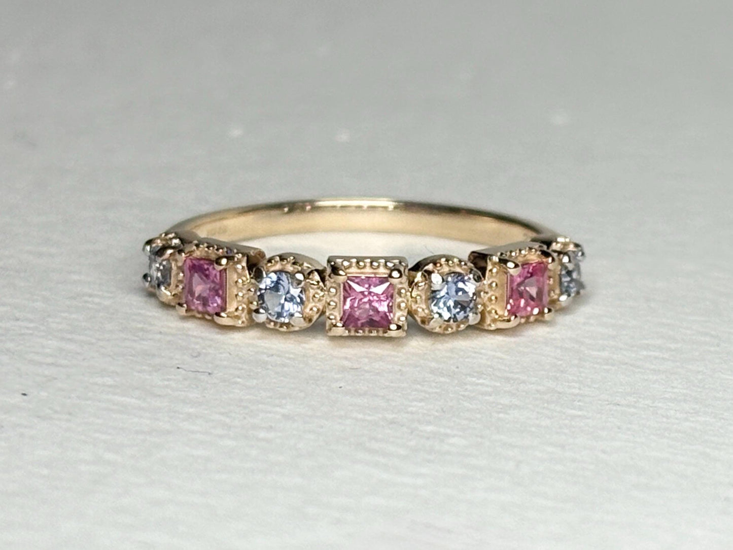 A 9k gold band ring with alternating pink princess cut and light violetish-blue round sapphires.
