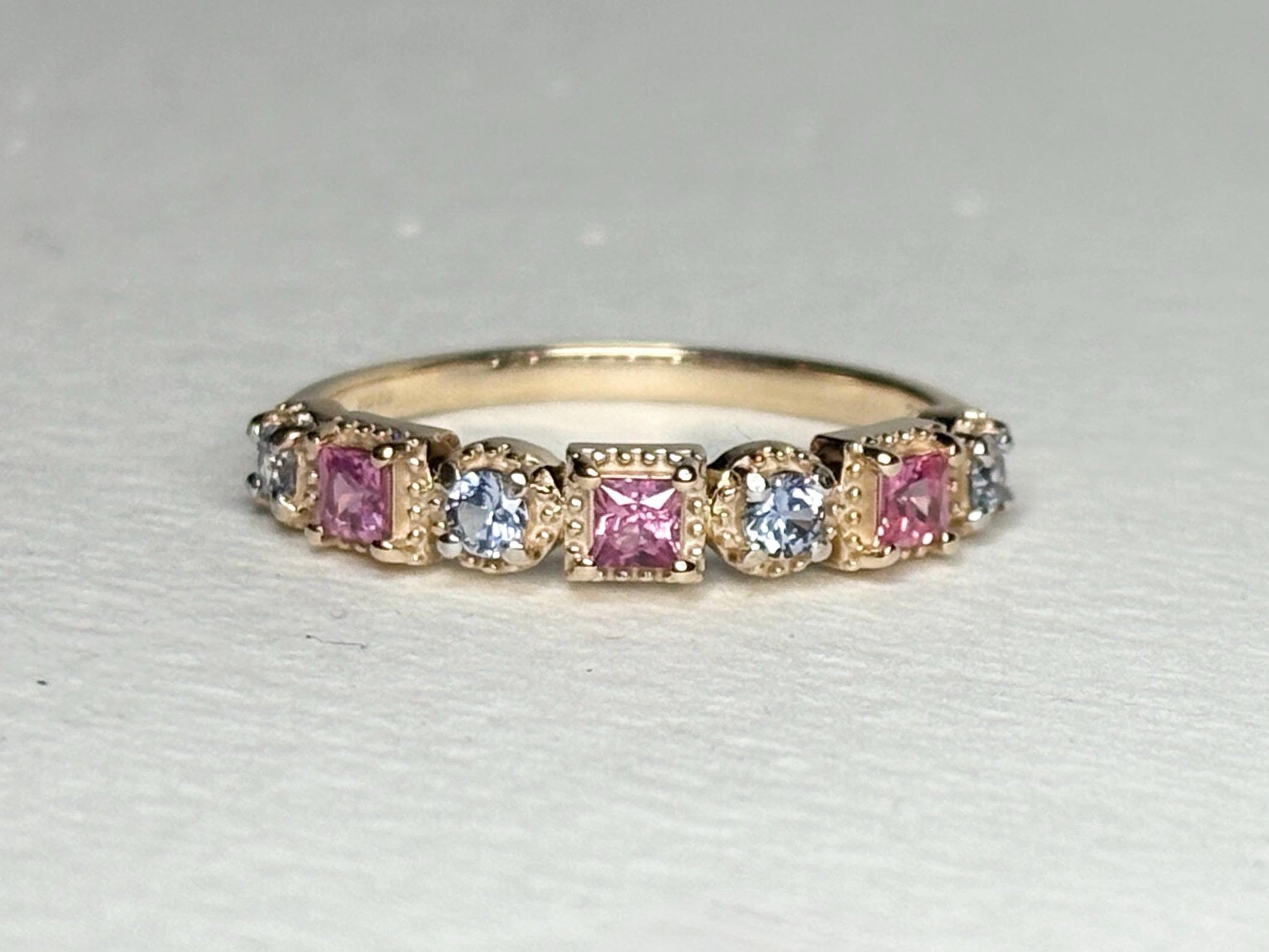 A 9k gold band ring with alternating pink princess cut and light violetish-blue round sapphires.