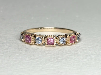 A 9k gold band ring with alternating pink princess cut and light violetish-blue round sapphires.