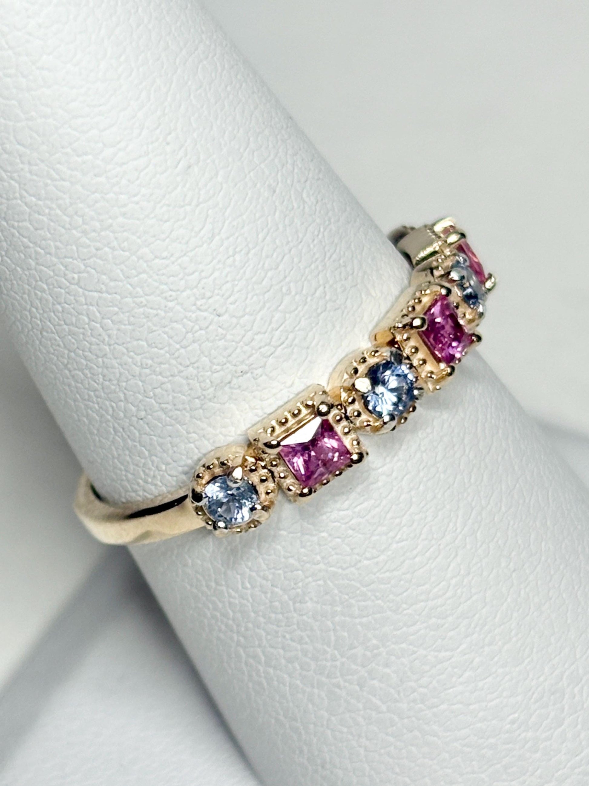 A 9k gold band ring with alternating pink princess-cut and light violetish-blue round sapphires.
