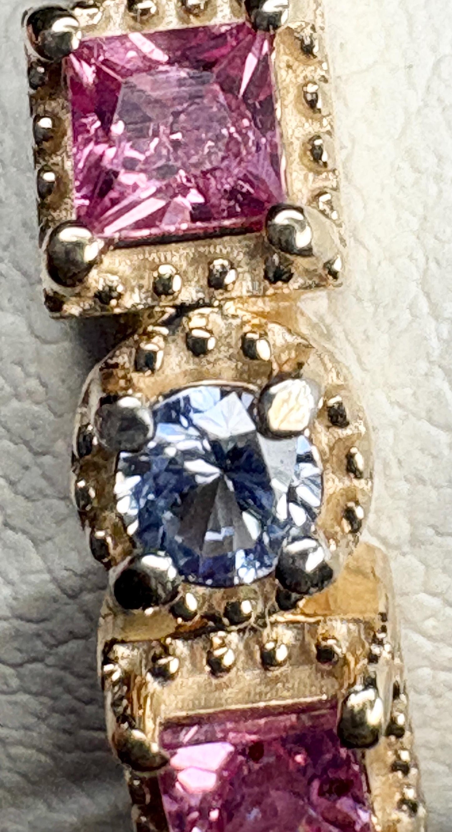 A 9k gold band ring with pink princess cut and light violetish blue round sapphires.