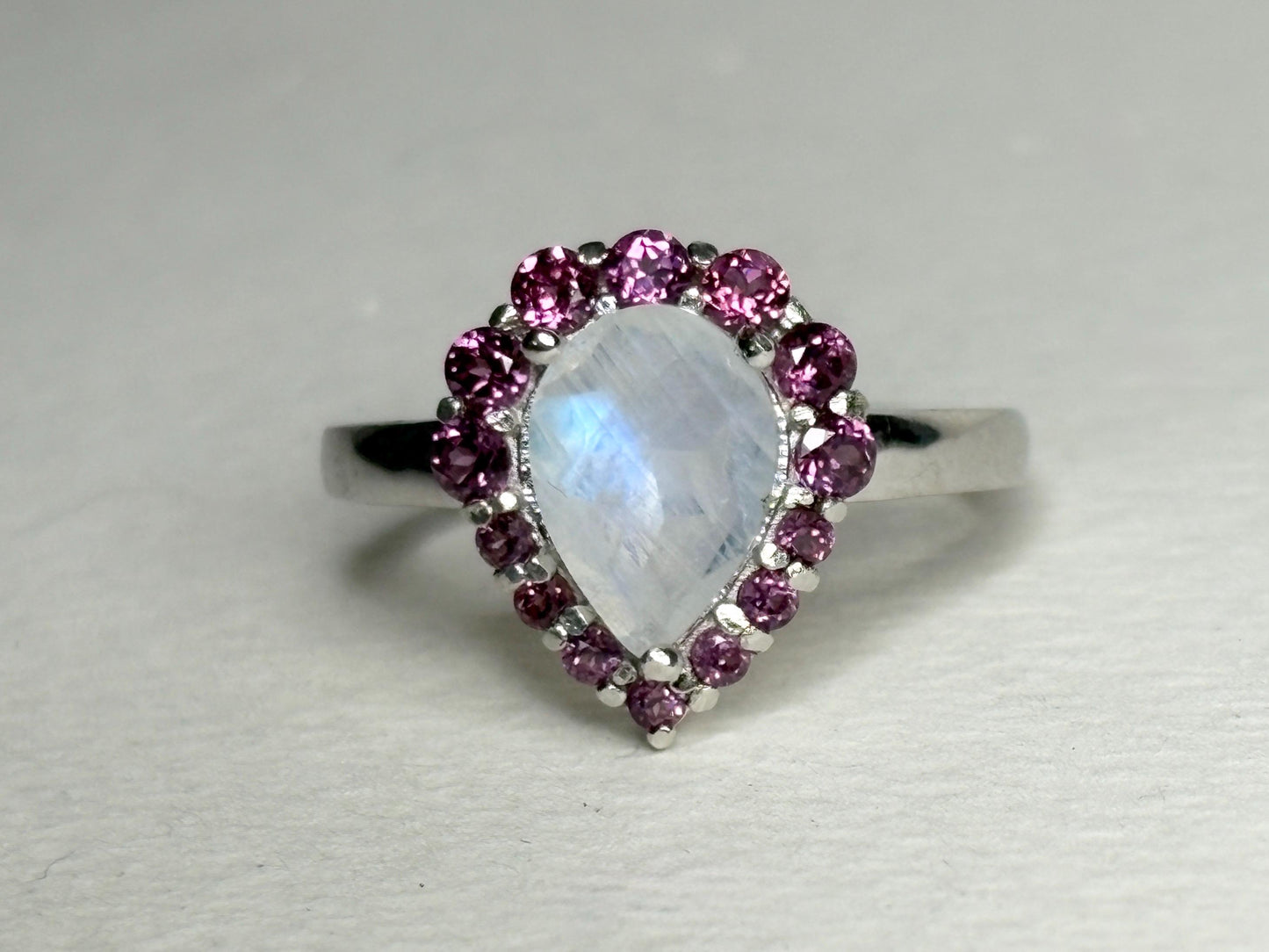 Sterling silver ring with a pear-shaped rainbow moonstone surrounded by rhodolite garnets.