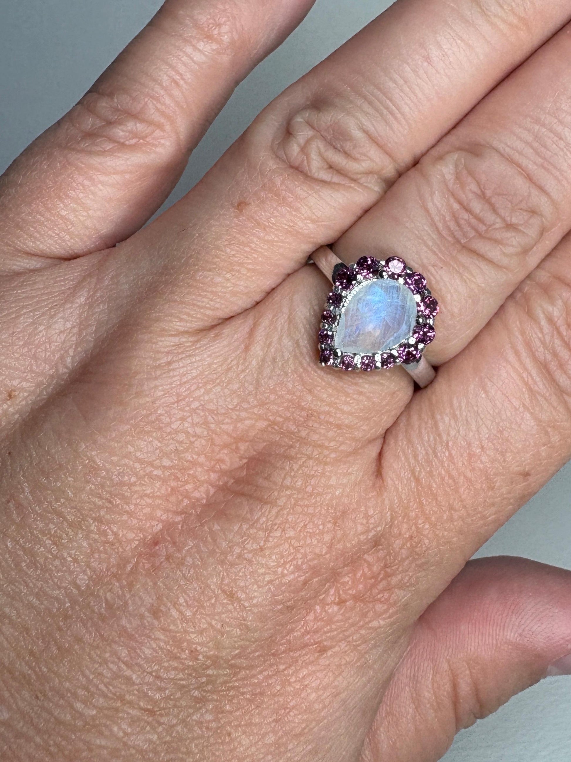 Sterling silver ring with a pear-shaped rainbow moonstone surrounded by rhodolite garnets.