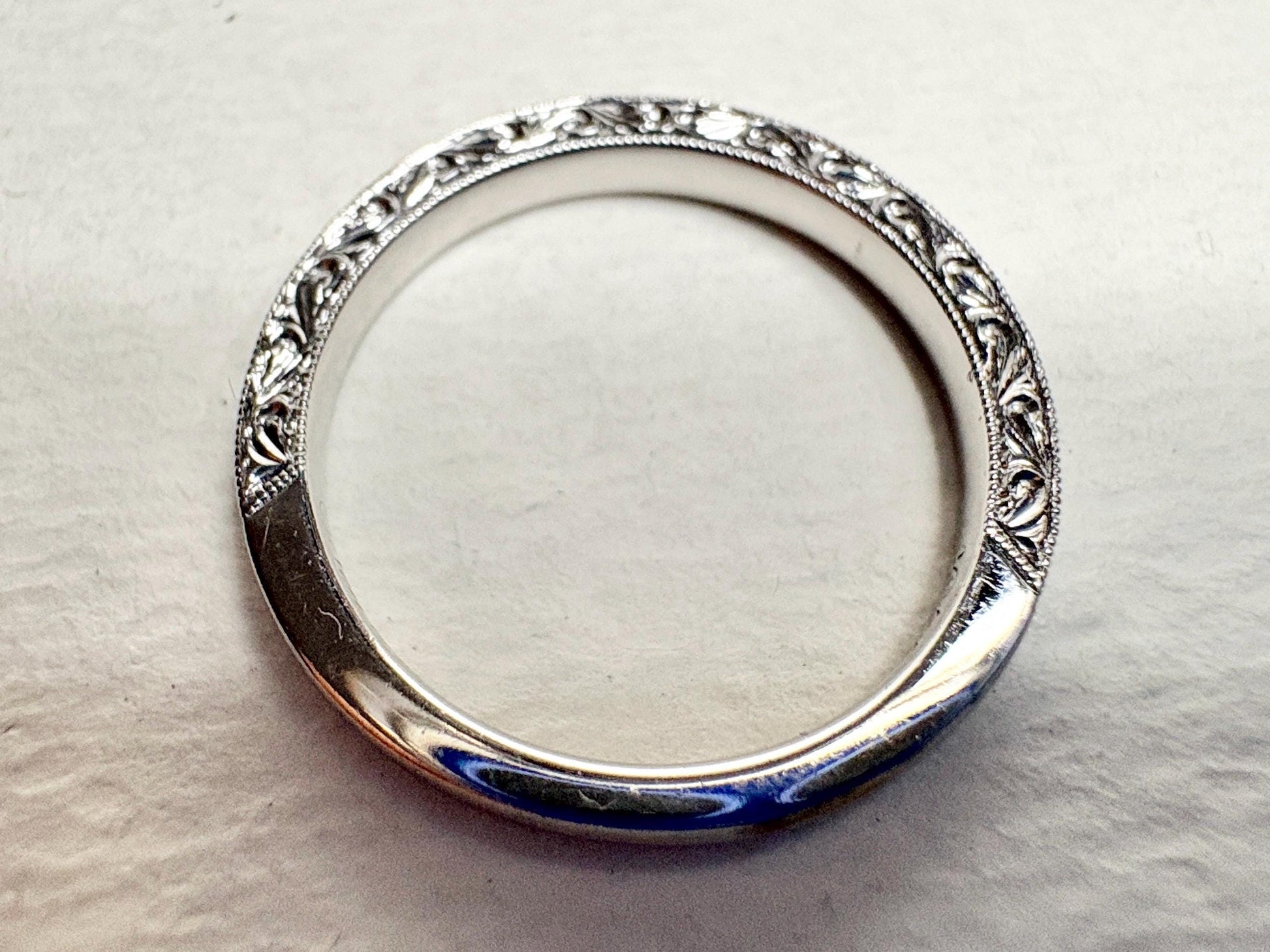 A white gold band ring with intricate detailing and diamonds.