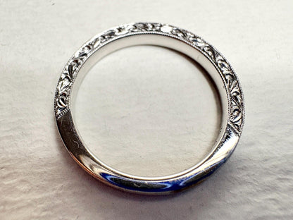 A white gold band ring with intricate detailing and diamonds.