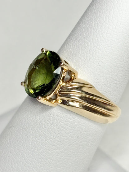 A size 7 solid 14k gold ring featuring an oval, faceted moldavite gemstone.