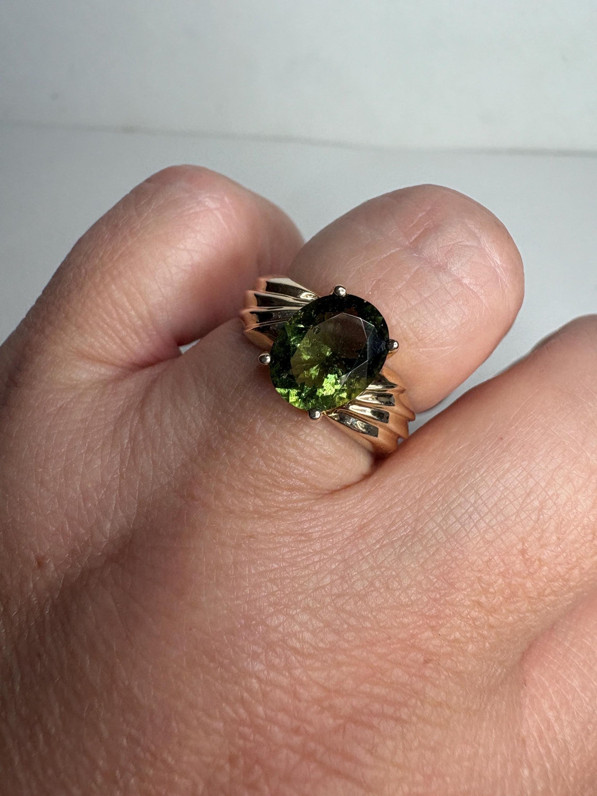 A size 7 solid 14k gold ring featuring an oval faceted moldavite gemstone.