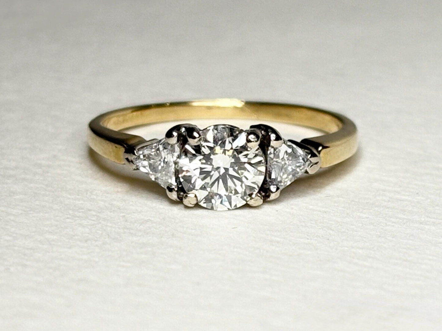 A round diamond engagement ring with two trillion diamonds on an 18k gold band.