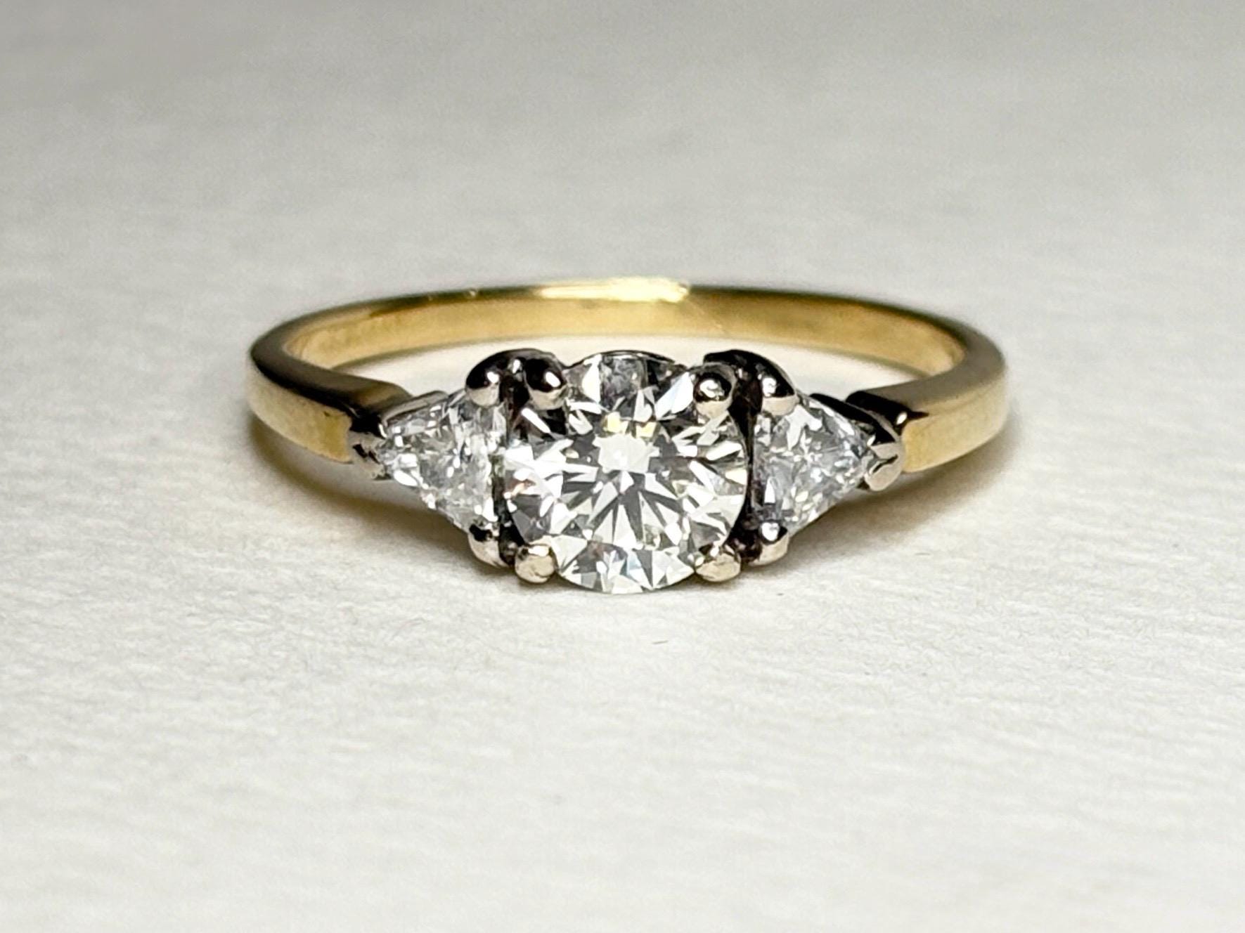 A round diamond engagement ring with two trillion diamonds on an 18k gold band.
