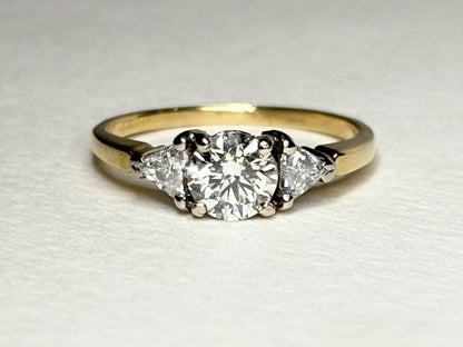 A round diamond engagement ring with two trillion diamonds on an 18k gold band.