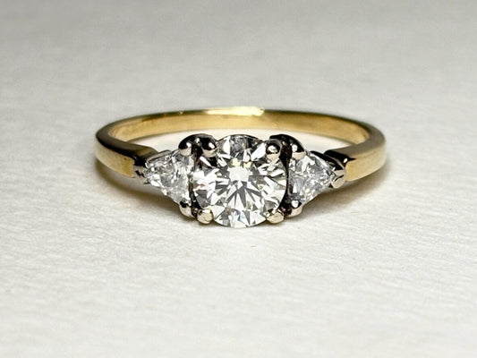 A round diamond engagement ring with two trillion diamonds on an 18k gold band.