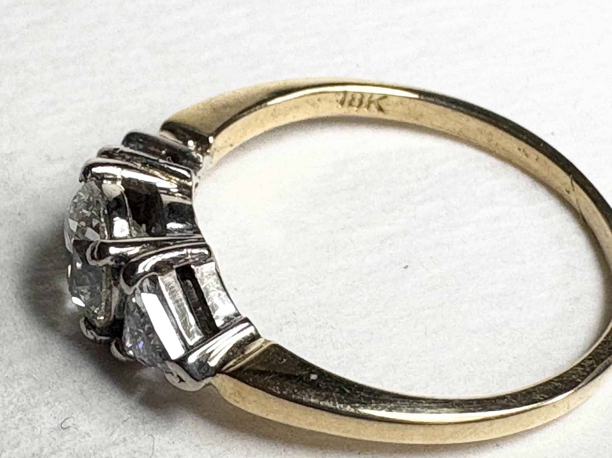 An 18k gold ring with three diamonds, including a central round diamond.
