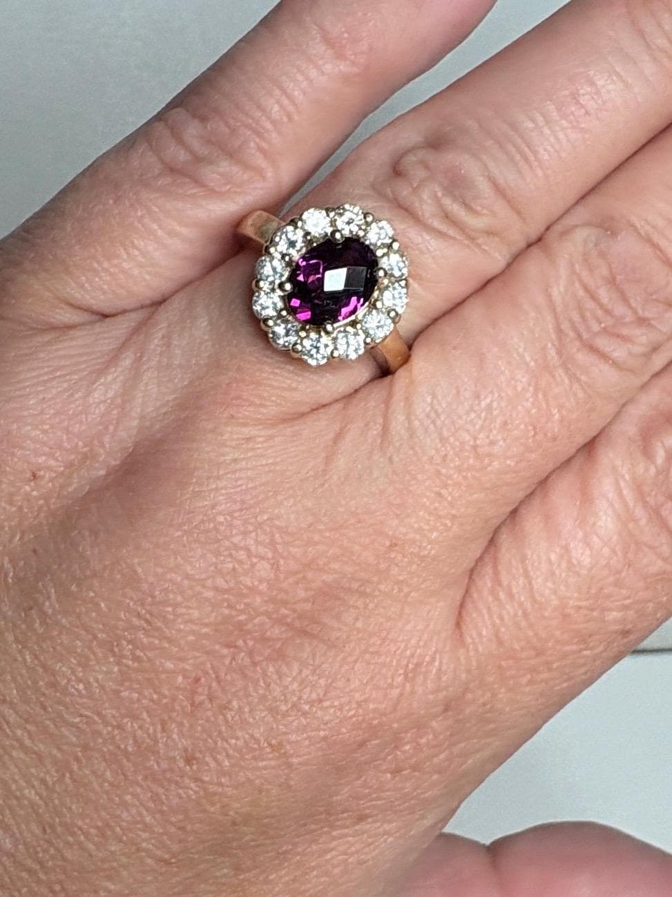 Oval checkerboard faceted rhodolite garnet halo ring with diamonds in yellow gold.