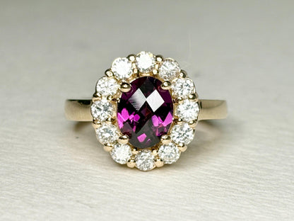 Oval checkerboard faceted rhodolite garnet ring surrounded by diamonds in a yellow gold halo setting.