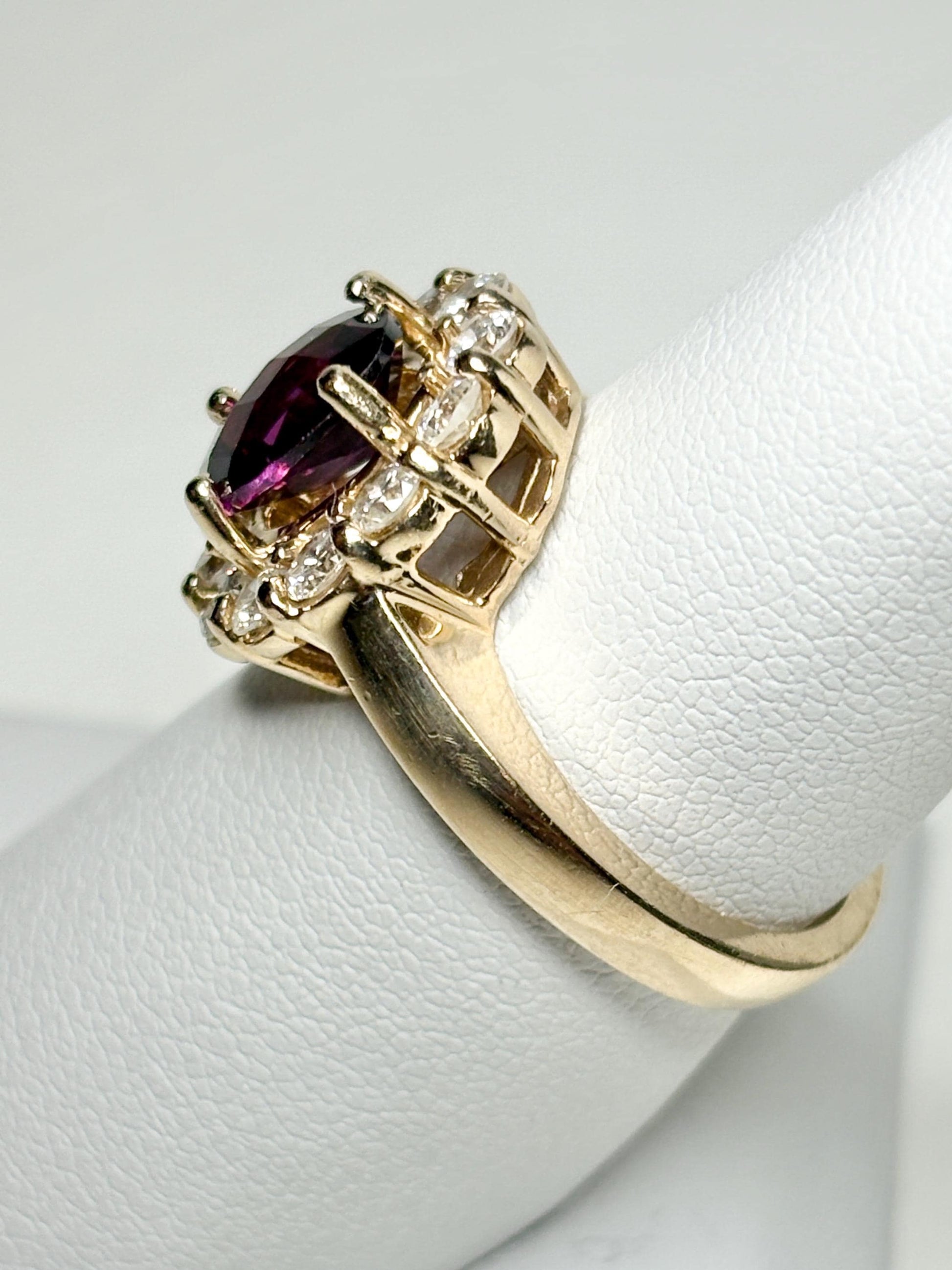 Gold ring with a checkerboard faceted rhodolite garnet center stone surrounded by diamonds.