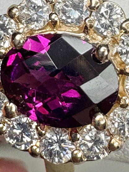 Oval checkerboard faceted rhodolite garnet ring surrounded by diamonds in a yellow gold halo setting.
