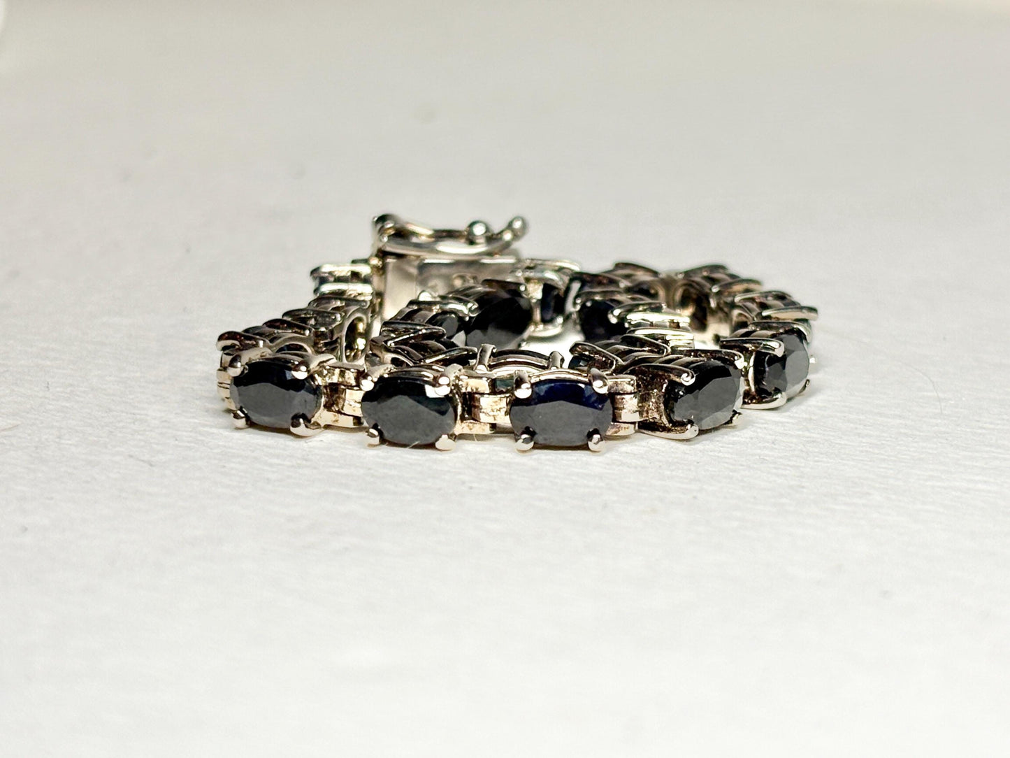 A tennis bracelet with oval dark blue sapphires set in silver-toned metal.