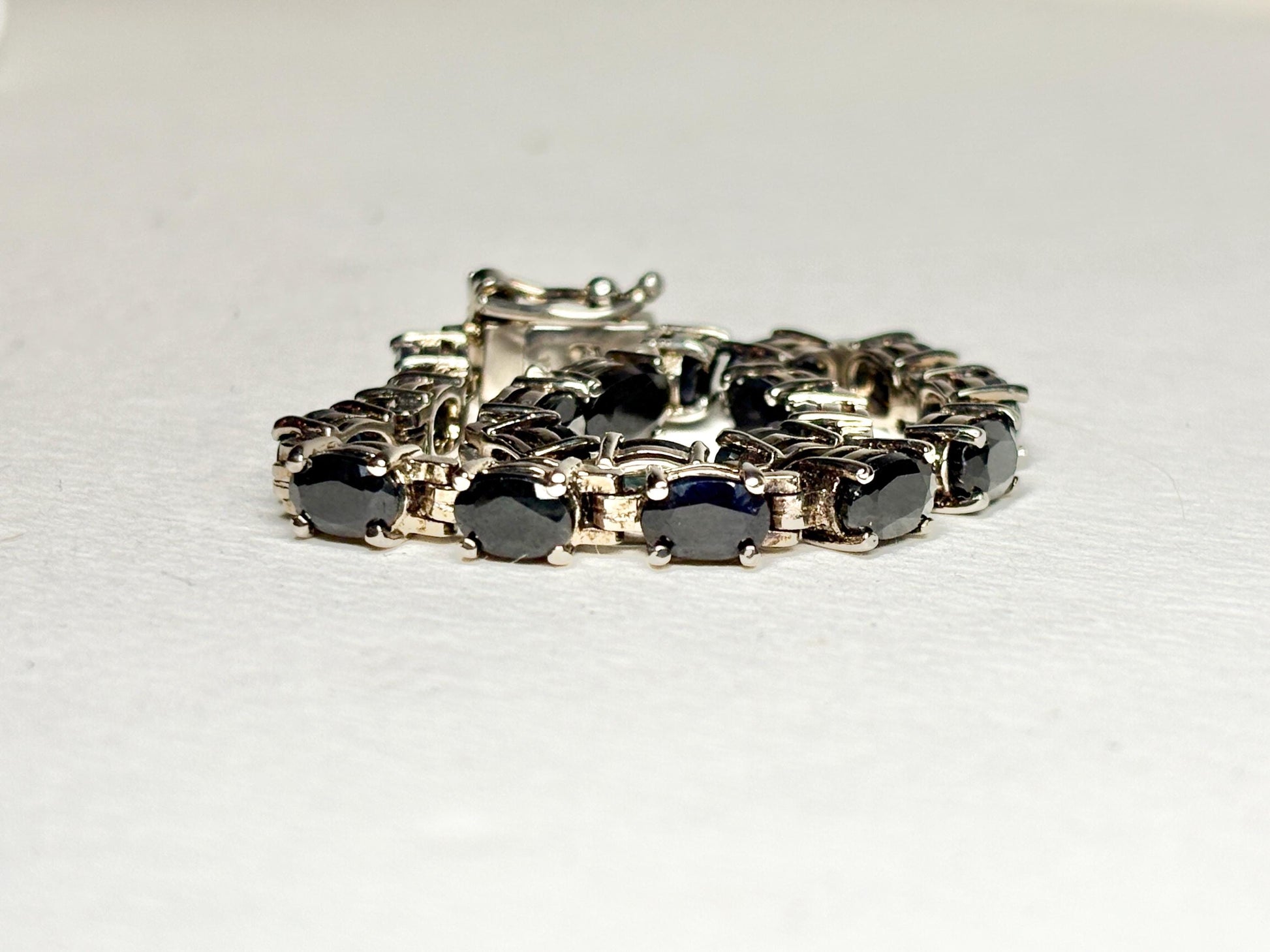 A tennis bracelet with oval dark blue sapphires set in silver-toned metal.