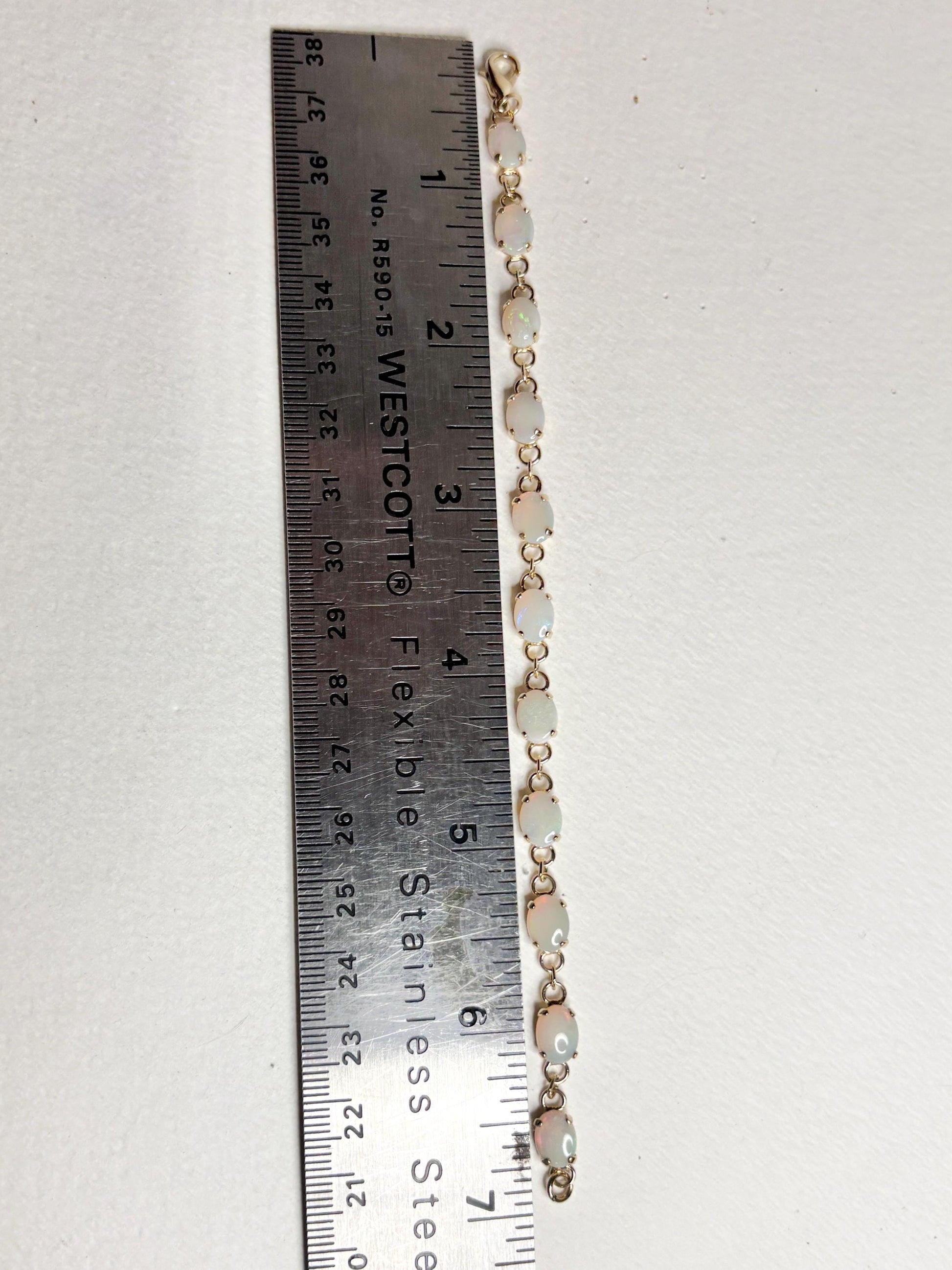 Gold plated tennis bracelet with 11 oval opals, measured against a ruler.