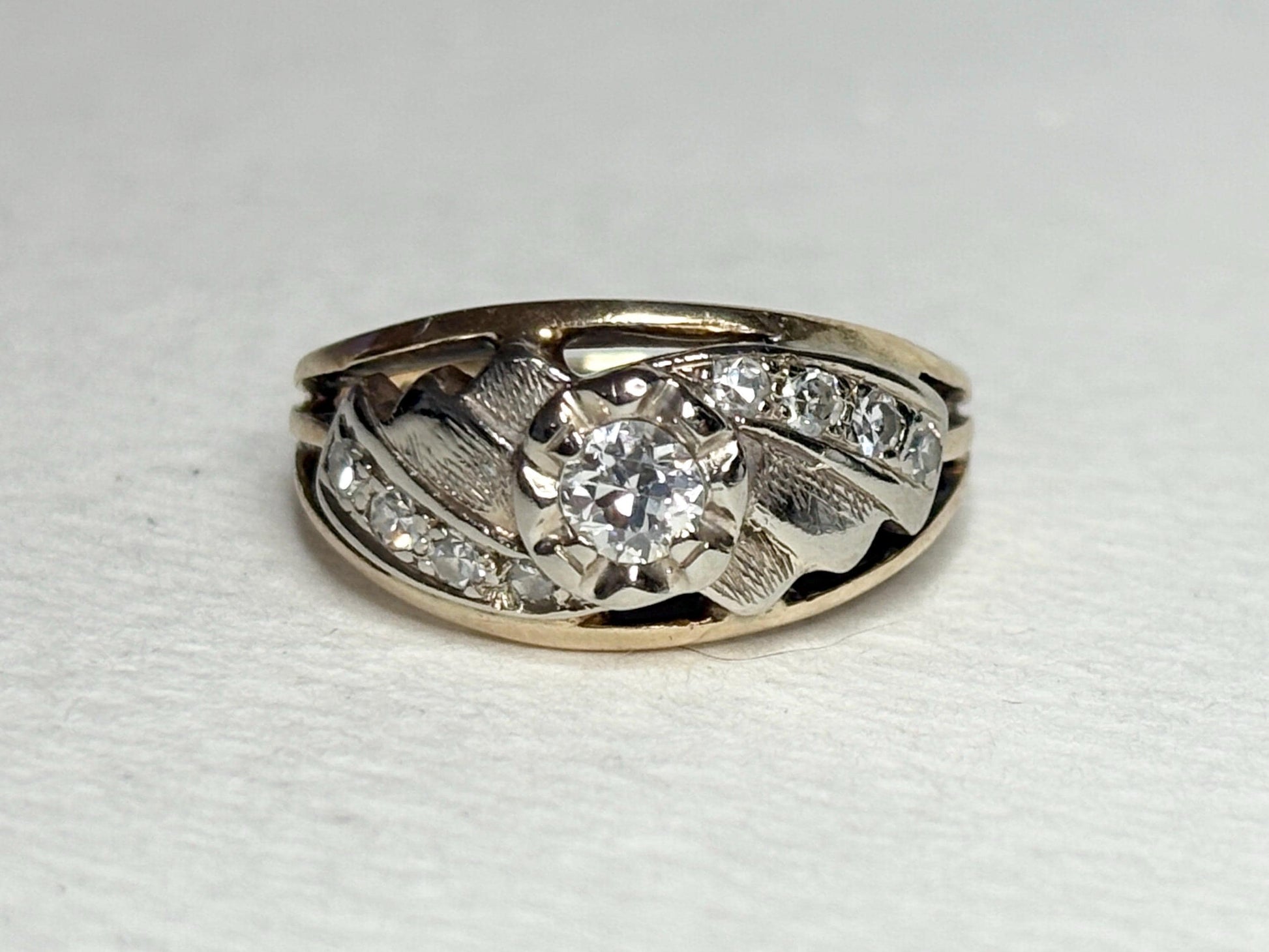 Mid-century two-tone 14k gold ring with a central diamond and smaller side diamonds.