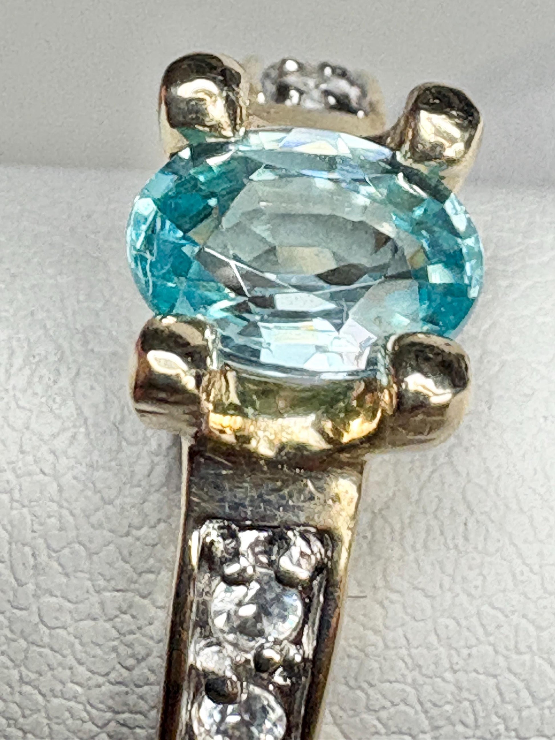 A two-tone 14k gold ring featuring an oval blue zircon and small clear side stones.