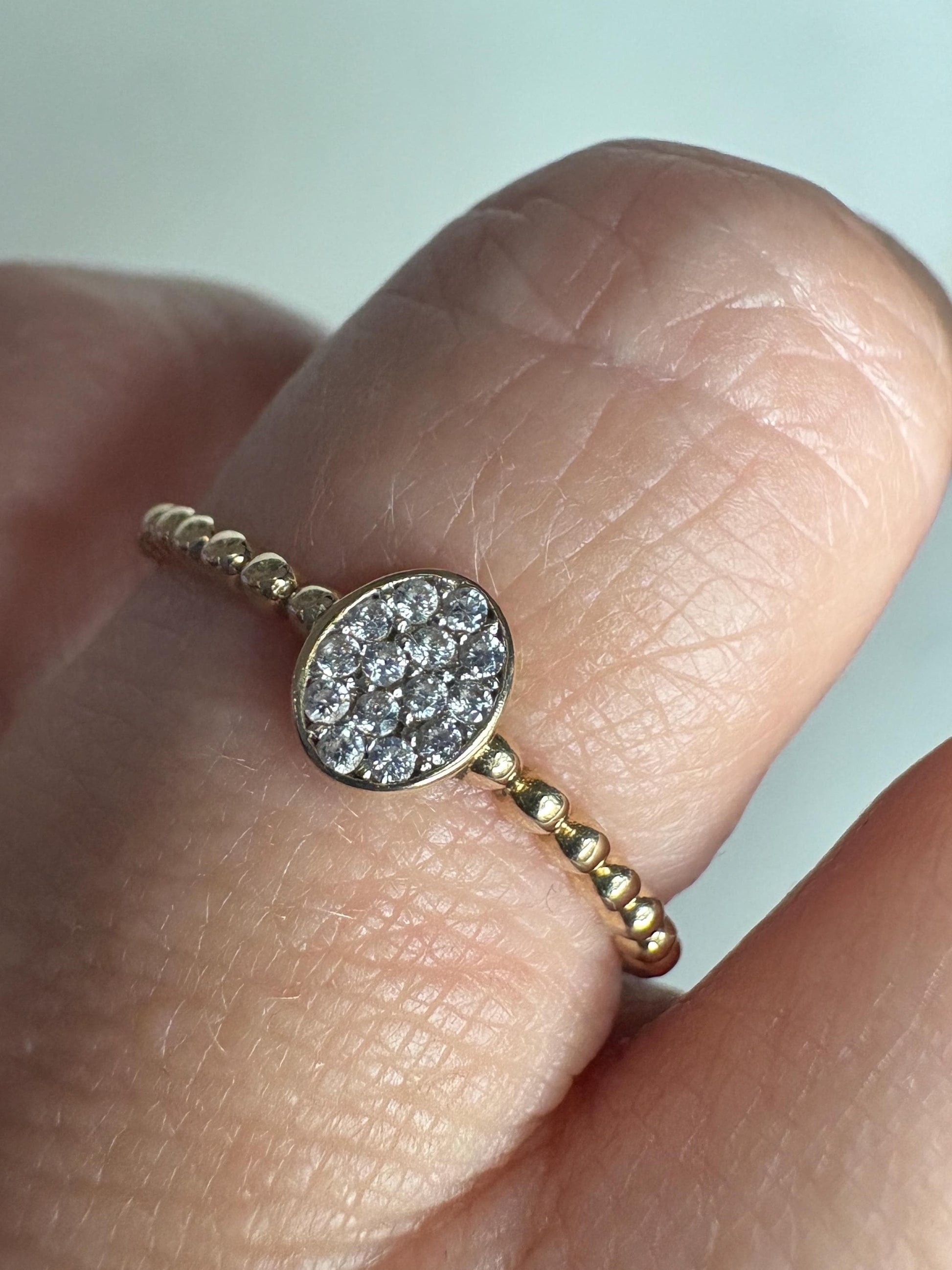 A dainty 14k gold ring with a beaded band and an oval pave-set crystal centerpiece.
