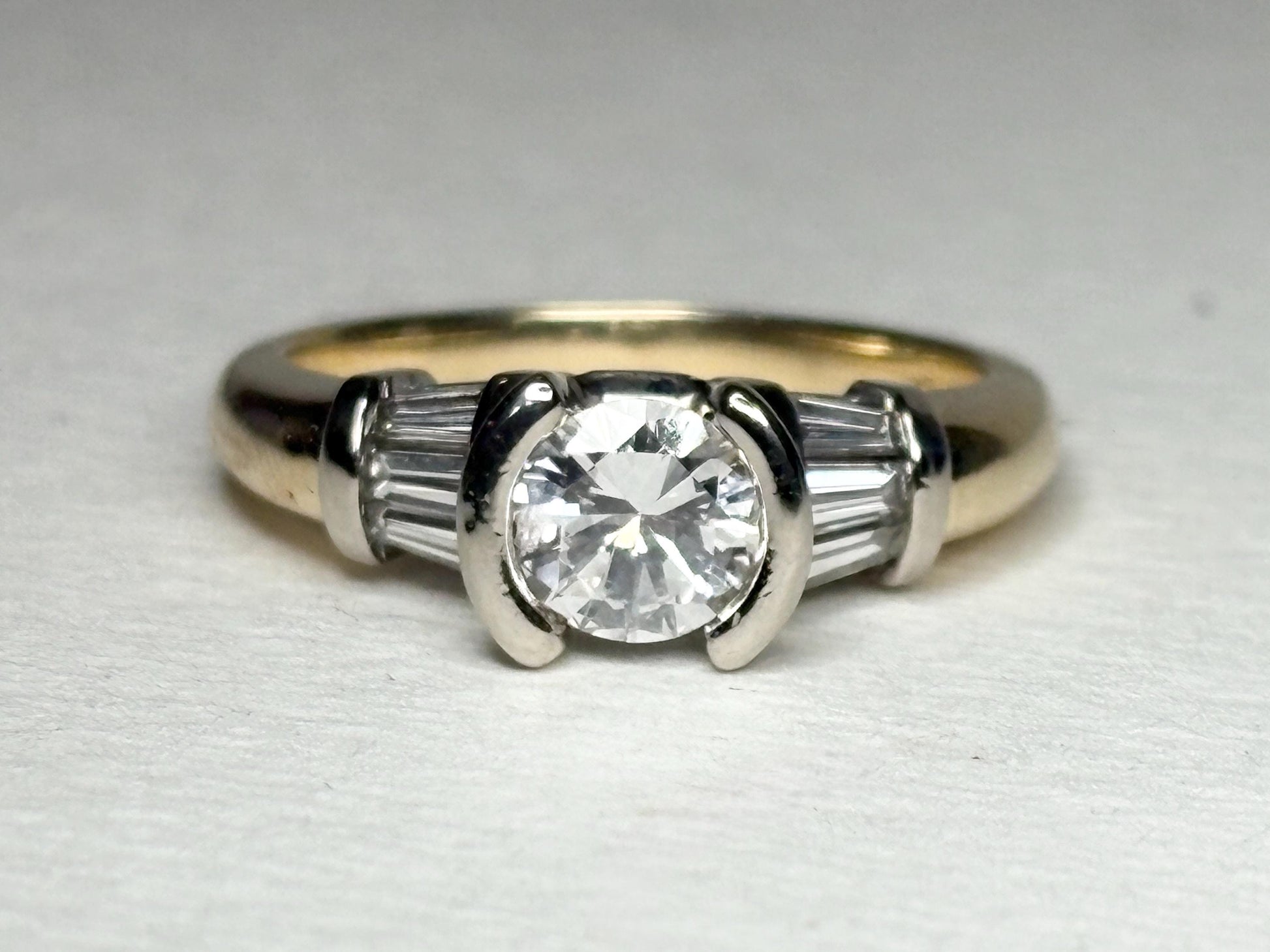A 14k two-tone gold ring with a round diamond and baguette side stones.