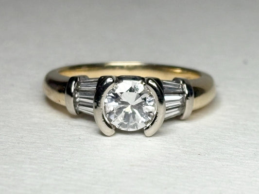 A 14k two-tone gold ring with a round diamond and baguette side stones.