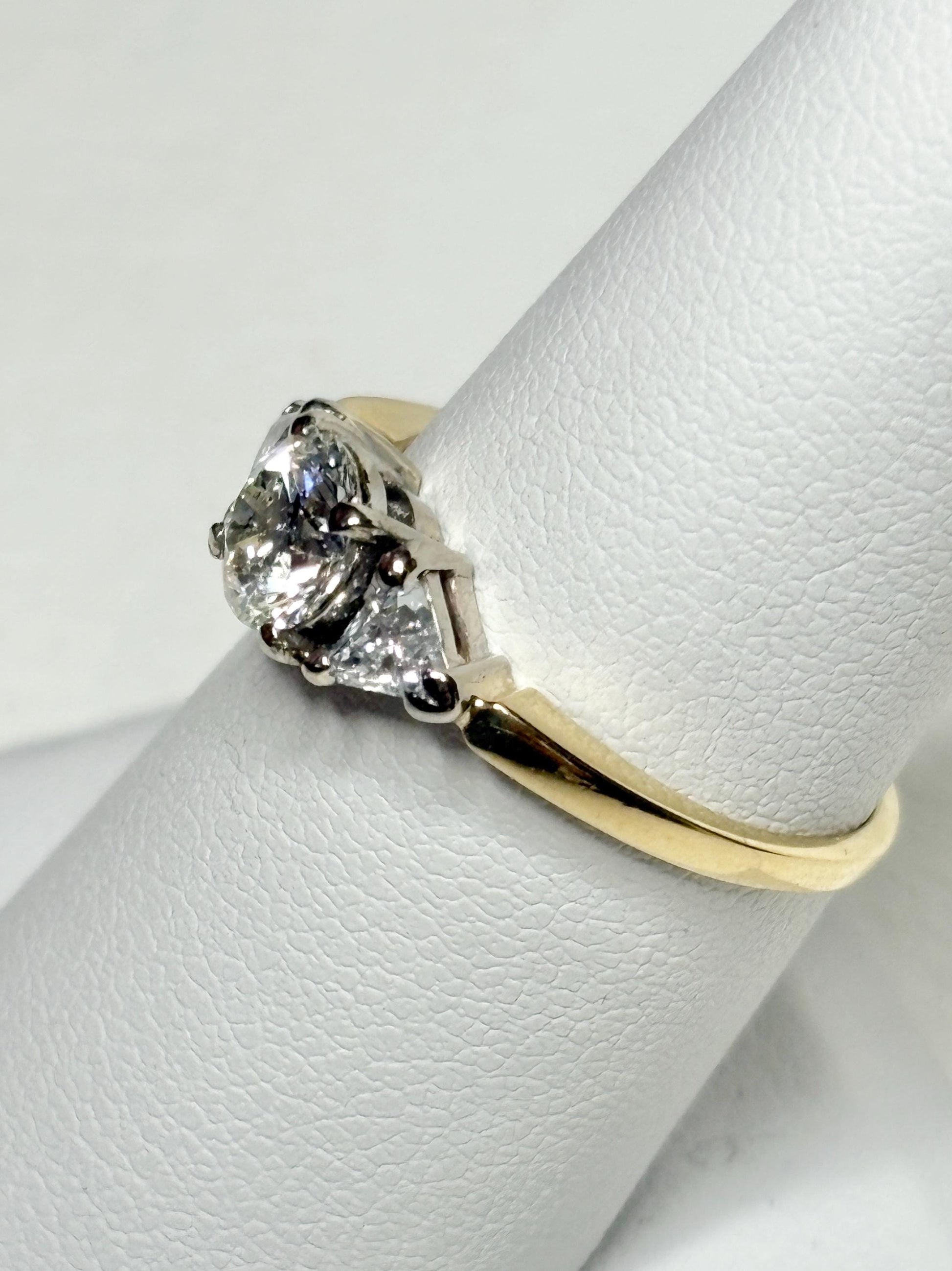 A gold ring with a round center diamond and two trillion side diamonds.