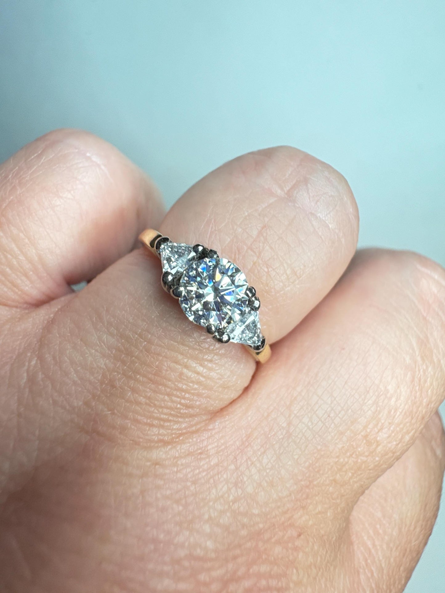 A gold ring with a round center diamond and two trillion side diamonds.