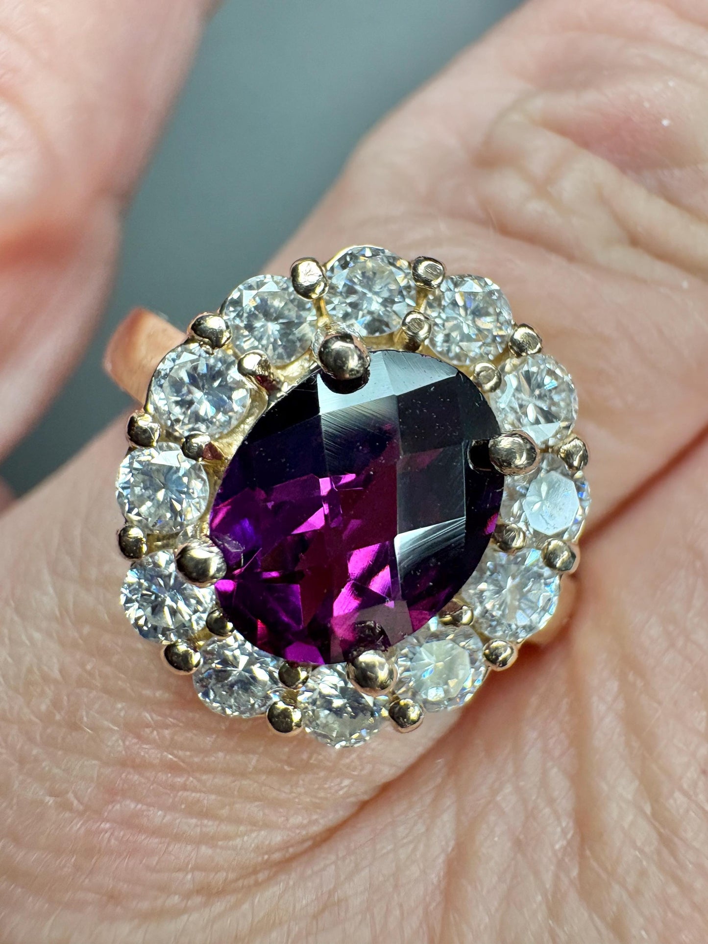 Oval checkerboard faceted rhodolite garnet ring surrounded by diamonds in a yellow gold halo setting.