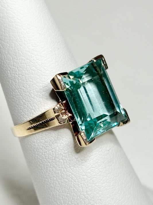 A vintage 10k gold ring with a rectangular mint paraiba colored synthetic spinel and orange blossoms.