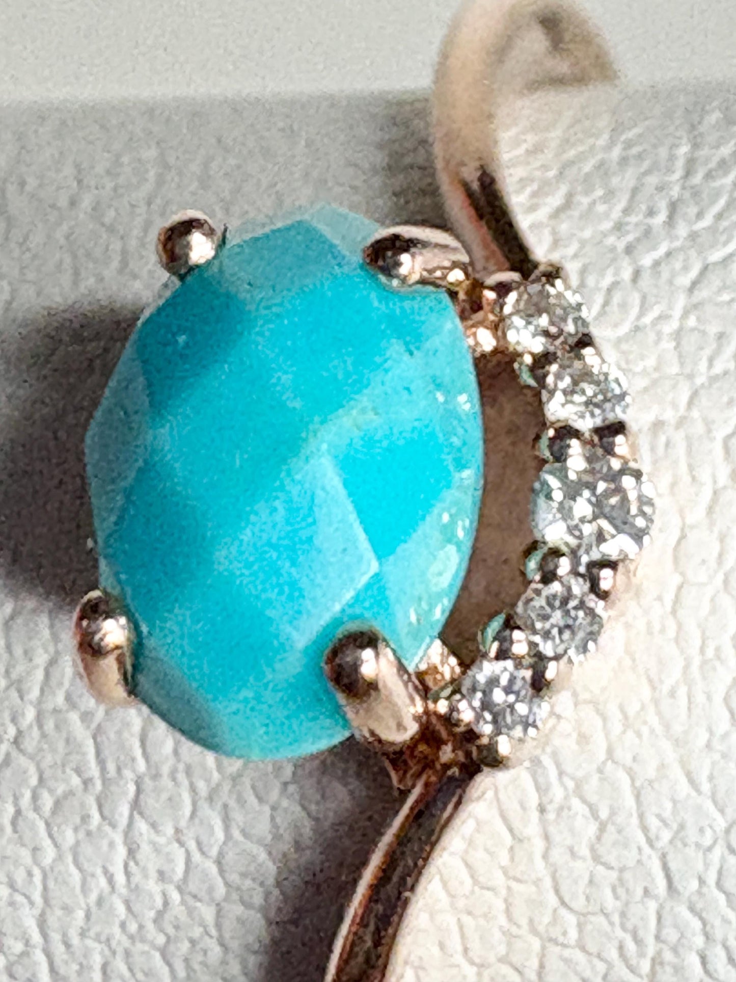 A checkerboard faceted turquoise oval is set in a rose gold ring with diamonds.