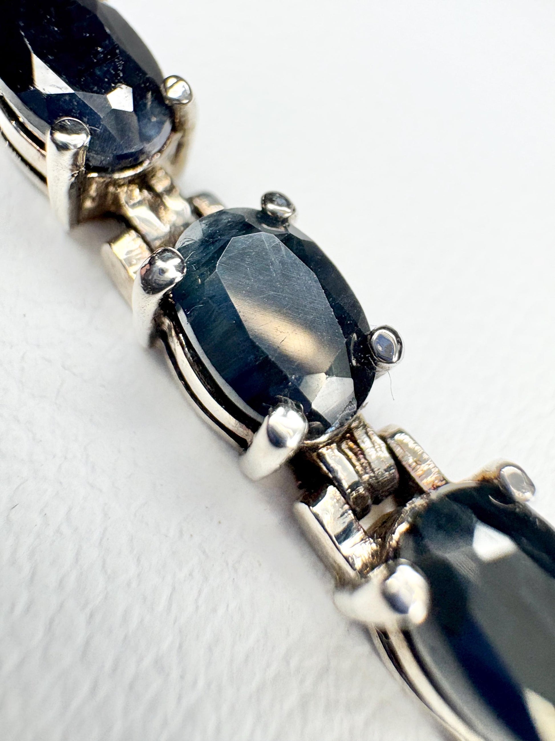 A tennis bracelet with oval dark blue sapphires and silver-toned metal.