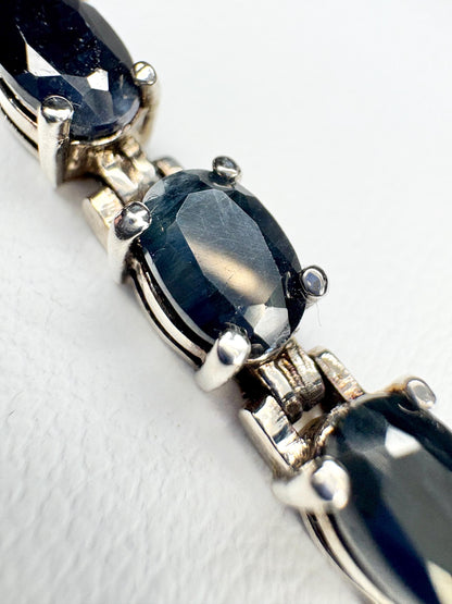 A tennis bracelet with oval dark blue sapphires and silver-toned metal.