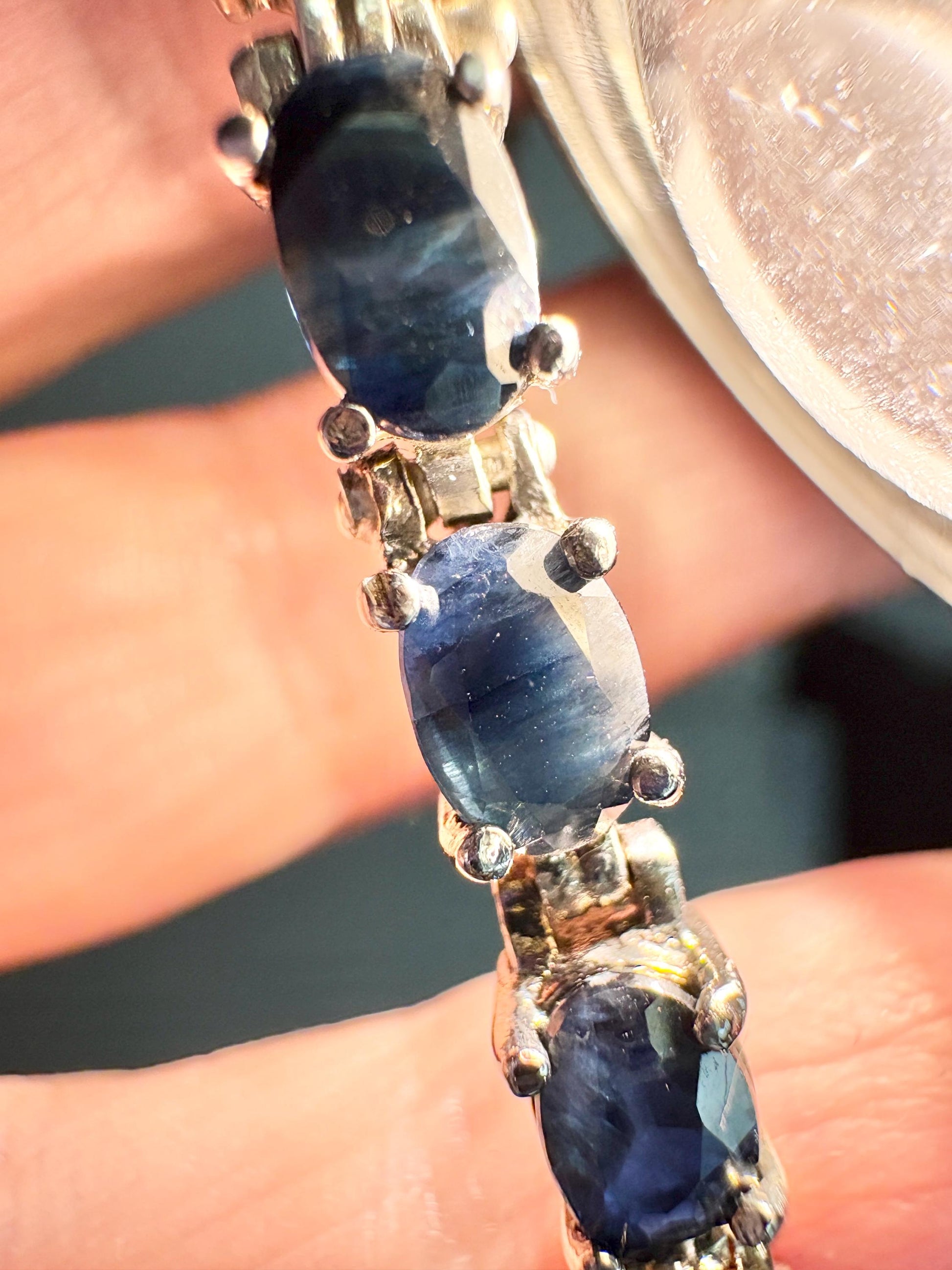 A tennis bracelet with oval dark blue sapphires set in stainless steel and sterling silver.