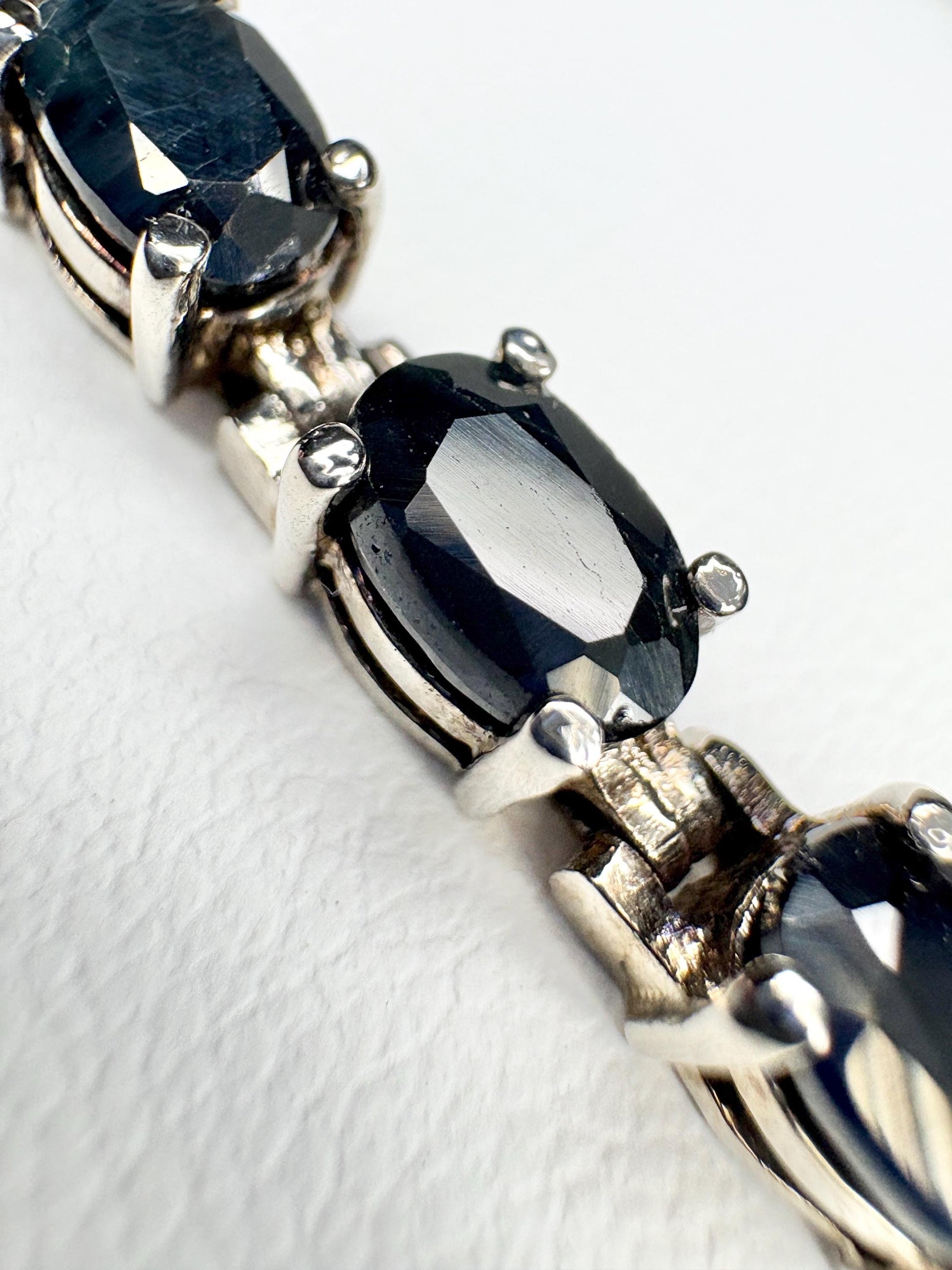 A sterling silver tennis bracelet with oval dark blue sapphires.