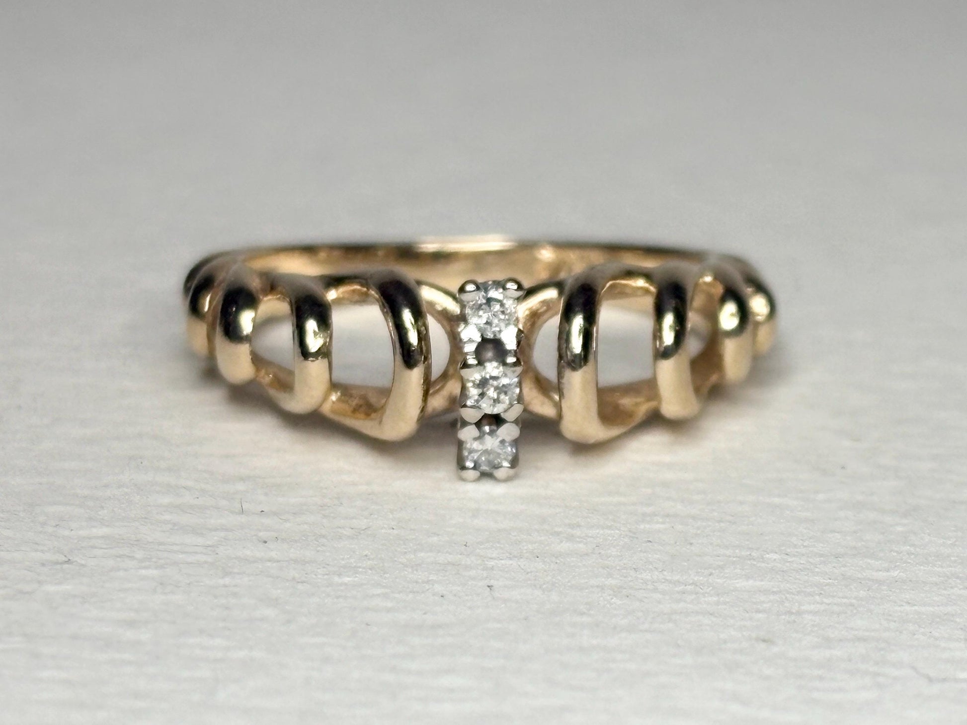 Vintage 14k gold band ring with ribbon loops and three small diamonds.