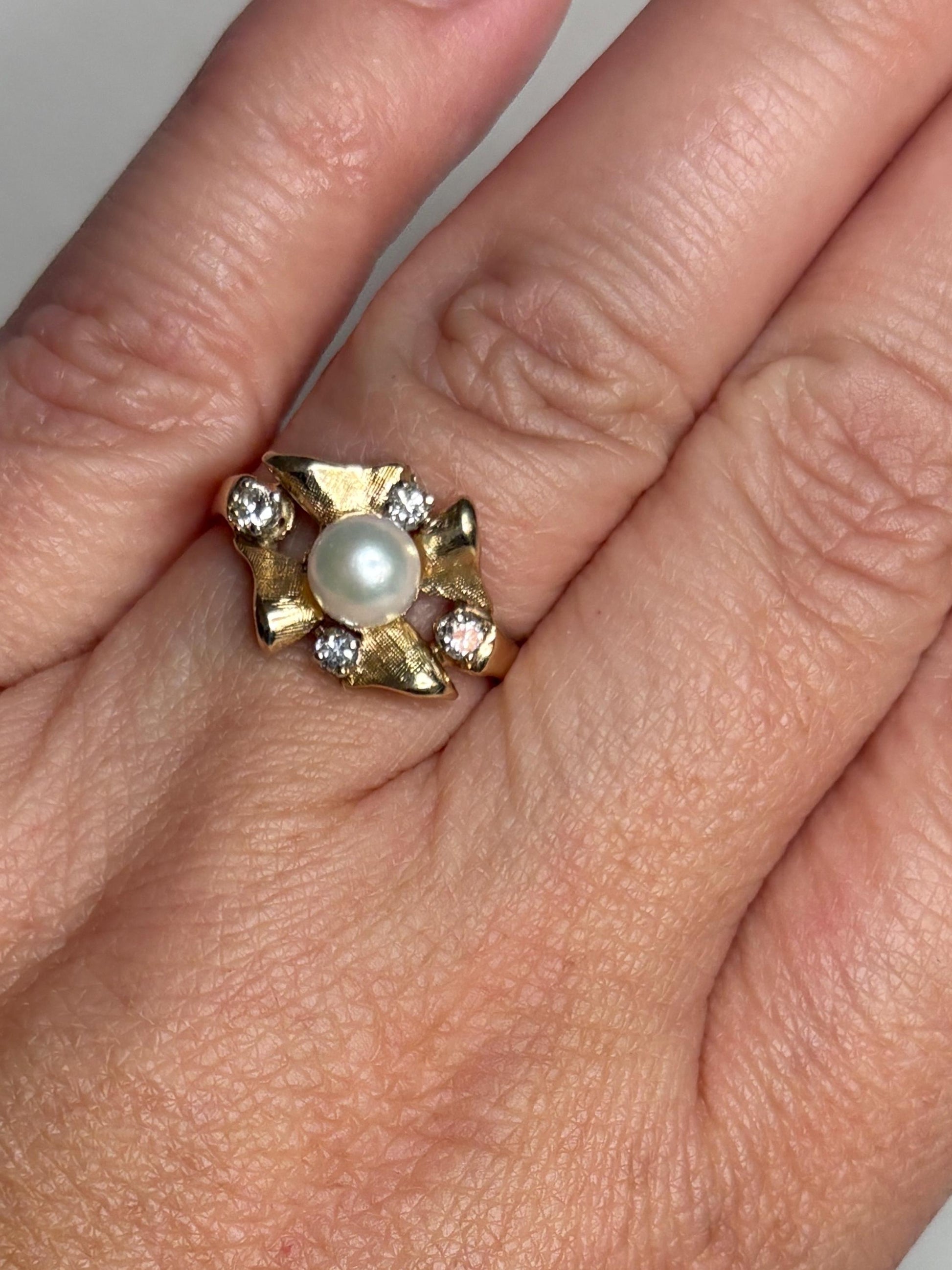 A 14k gold ring with a pearl and diamonds in a bow design.
