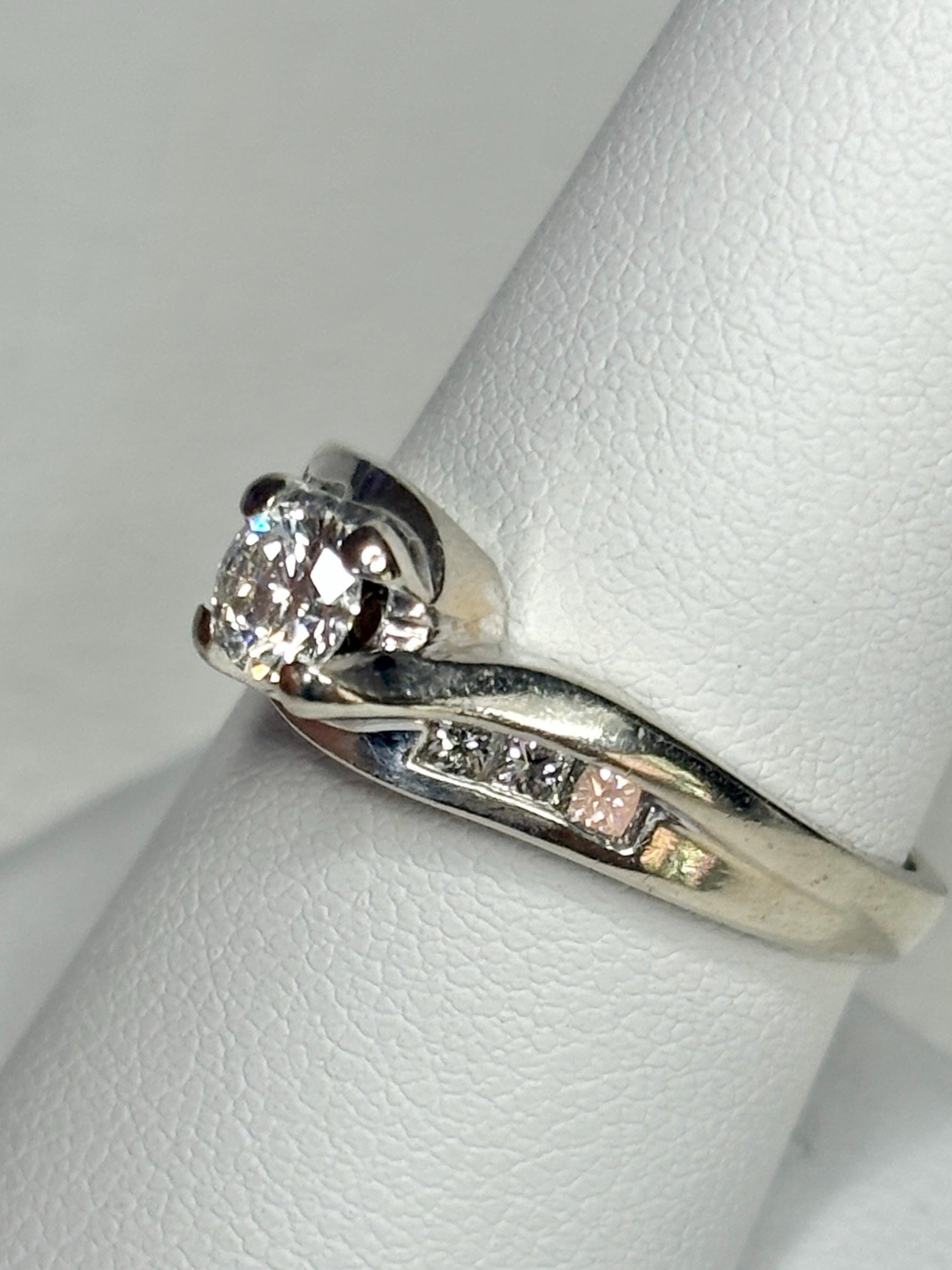 A vintage 14k white gold engagement ring with a central diamond and channel-set accent diamonds.
