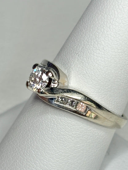 A vintage 14k white gold engagement ring with a central diamond and channel-set accent diamonds.