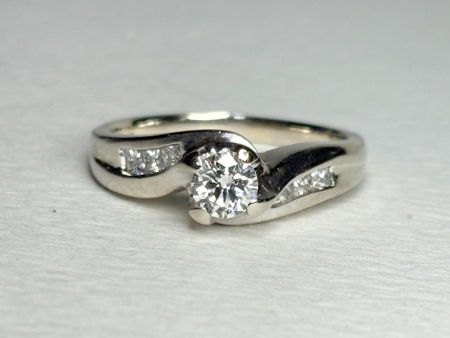 A vintage 14k white gold engagement ring with a central diamond and channel-set princess cut diamonds.