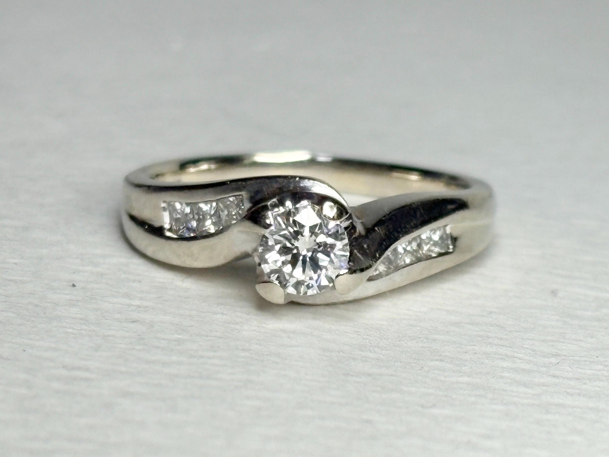 A vintage 14k white gold engagement ring with a central diamond and channel-set princess cut diamonds.