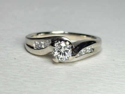 A vintage 14k white gold engagement ring with a central diamond and channel-set princess cut diamonds.
