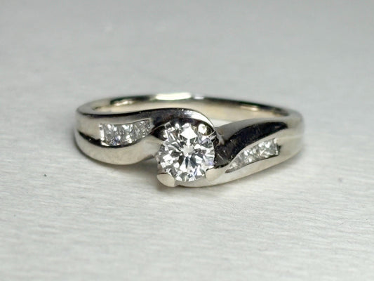 A vintage 14k white gold engagement ring with a central diamond and channel-set princess cut diamonds.