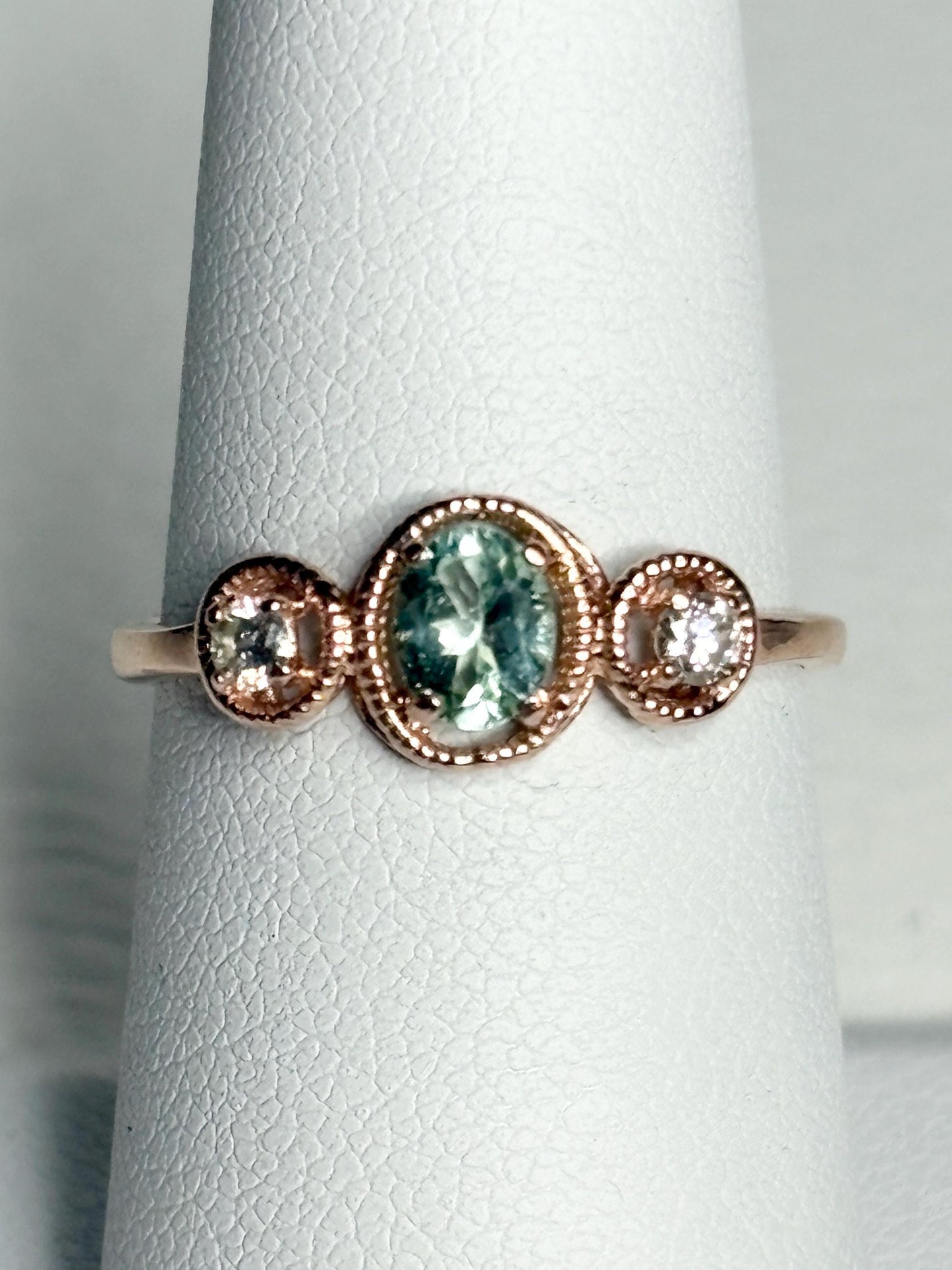 14k rose gold ring with a central oval Paraiba colored tourmaline and two side diamonds.