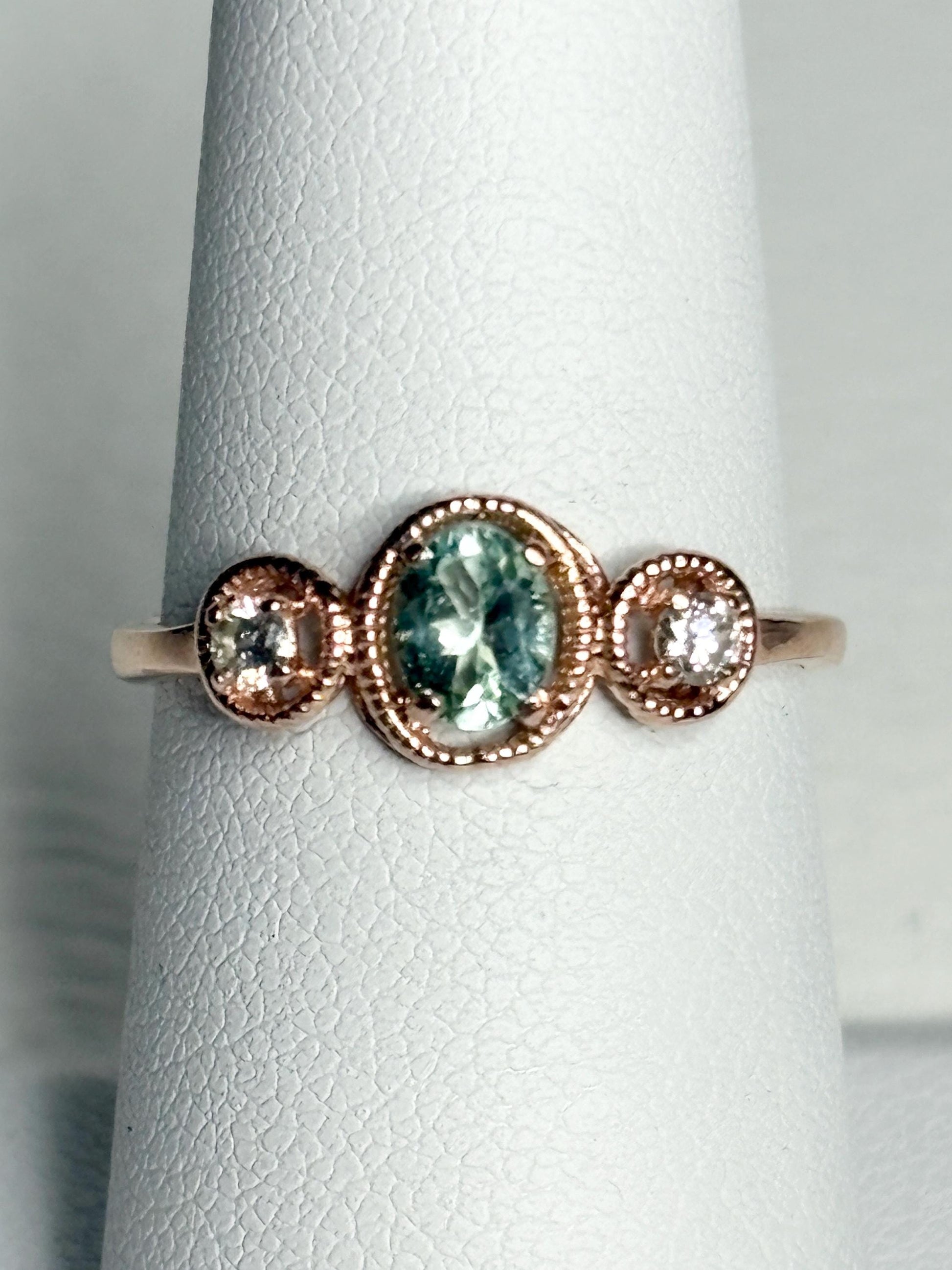 14k rose gold ring with a central oval Paraiba colored tourmaline and two side diamonds.