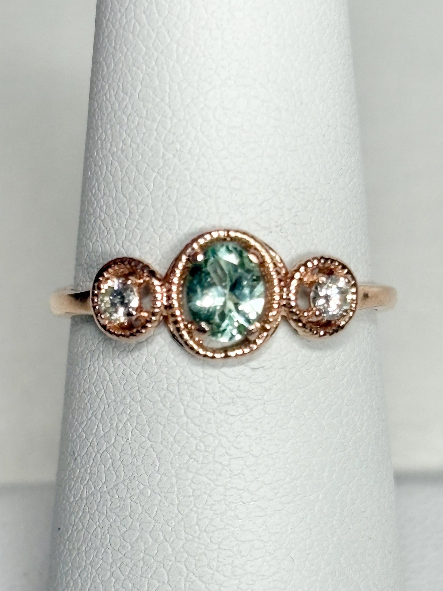 14k rose gold ring with a central oval Paraiba colored tourmaline and two side diamonds.