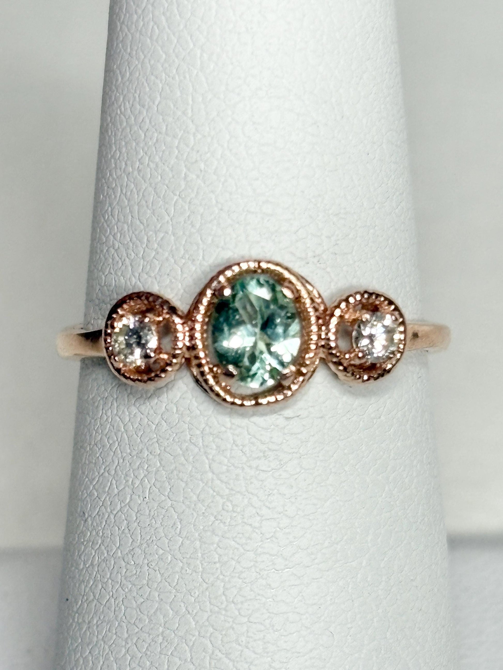14k rose gold ring with a central oval Paraiba colored tourmaline and two side diamonds.