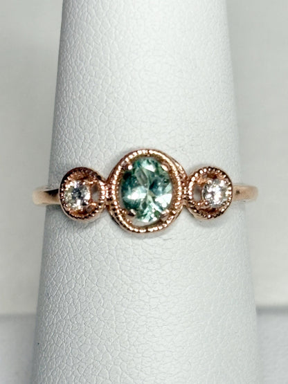 14k rose gold ring with a central oval Paraiba colored tourmaline and two side diamonds.